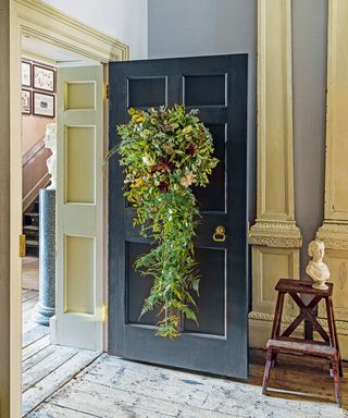 A large door wreath with trailing foliage with ferns, jasmine, ivy and mimosa, hanging on a black interior door.