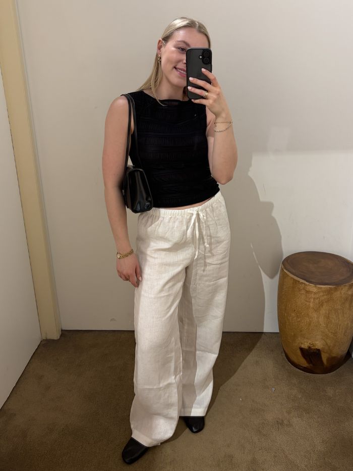 Woman wears black top, black bag, white linen trousers and ballet flats