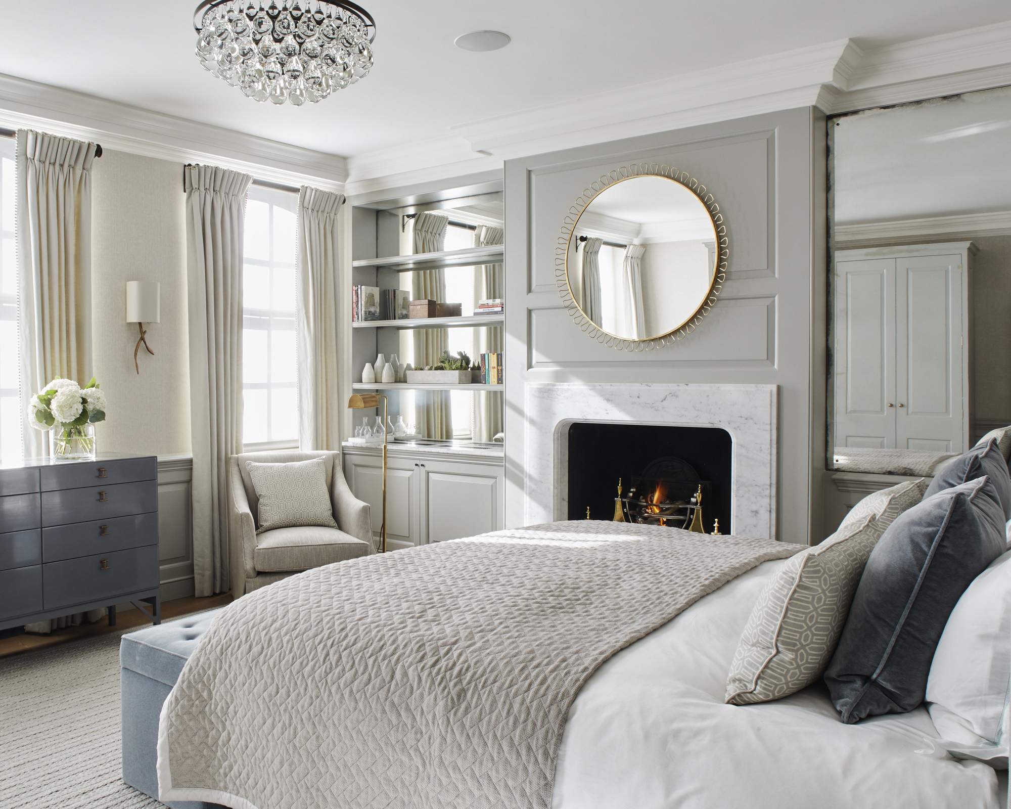 A grey bedroom idea with pale grey wall panels and large mirror over a marble fireplace