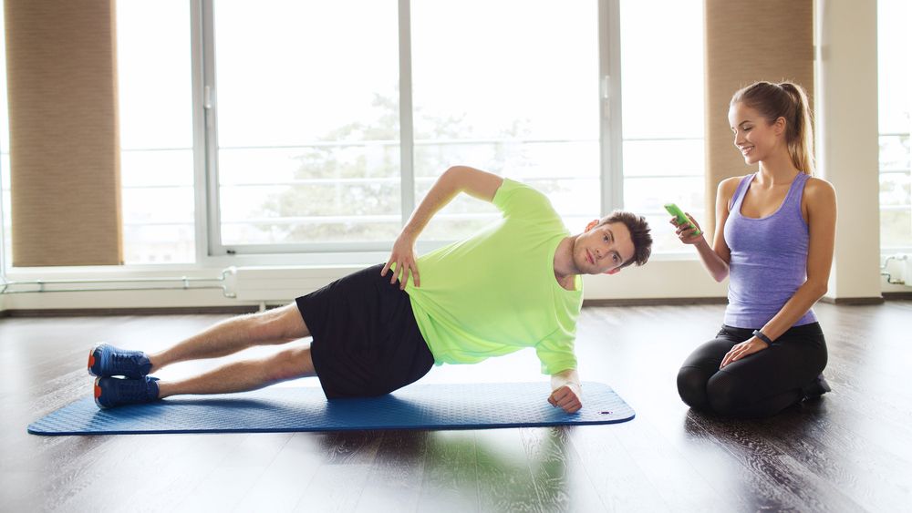 Man holds a side plank while a woman times him