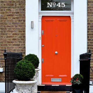 front door colour ideas, traditional house exterior with orange front door and number above, planters and railings, tiled path and steps