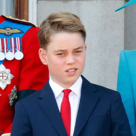 Prince George wears a navy suit with a red tie and stands on the balcony with his family