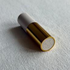 Image showing the Violette FR Bisou Balm in the shade laying at an angle against an off-white linen background 