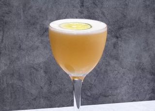a light-brown cocktail in a Nick and Nora glass against a slate-grey backdrop