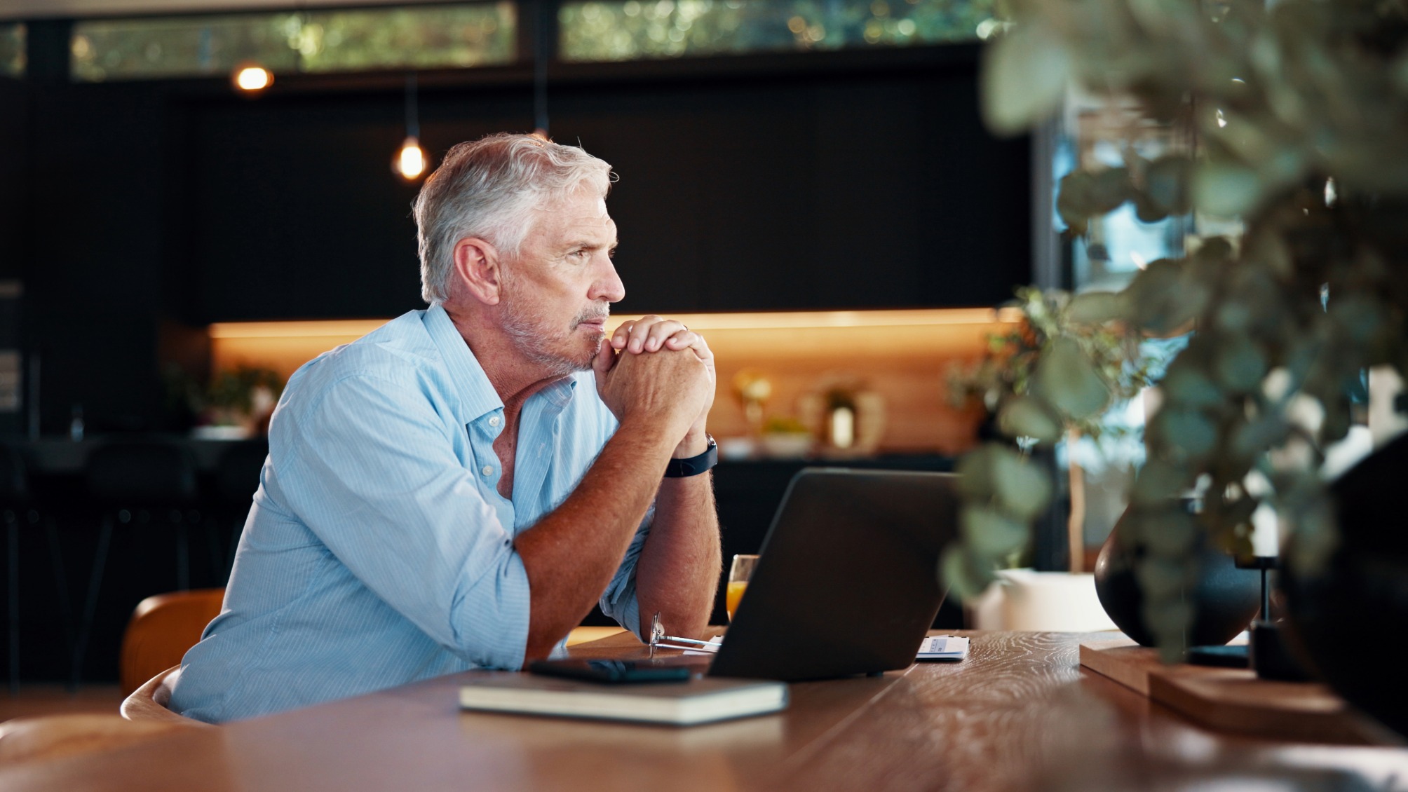 Portrait of thoughtful mature man with laptop sitting at wooden table 