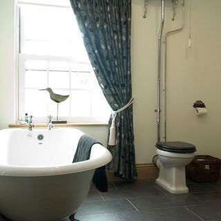 bathroom with white wall and bathtub with commode and curtain on window