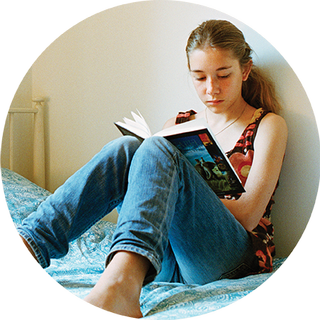 Young girl sitting on her bed, reading a book