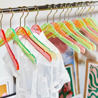 Cool neon green and pink clothes hangers on rail with colorful and patterned artwork on floor