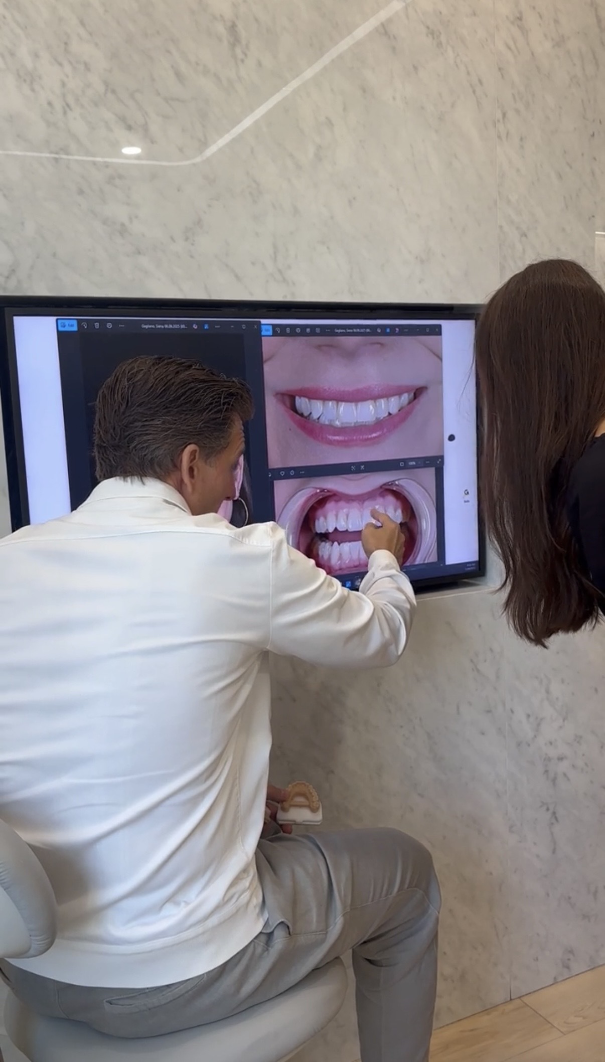 Dentist with a white coat pointing to images on a TV screen that depict teeth next to a girl with long brown hair