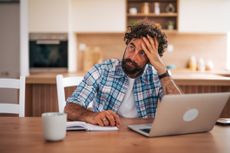 Tired freelancer or man his 40s holding his head in frustration while working from home, , embodying the stress and exhaustion of remote work or underemployement.
