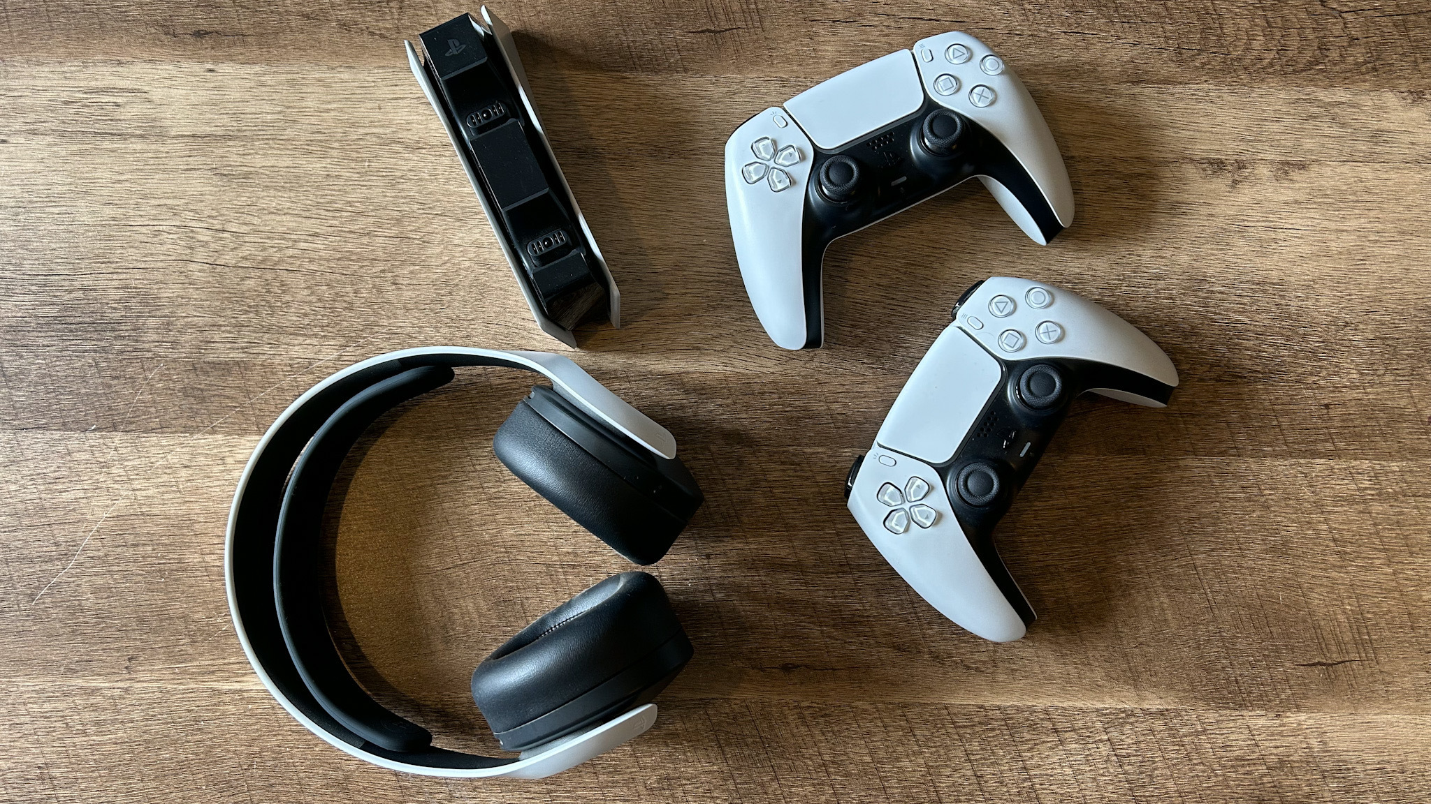 PS5 accessories on a table, including two DualSense controllers, a charging station and a headset