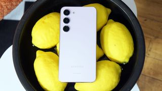 Samsung Galaxy S23 Plus i vitt, med framsidan vänd nedåt i en skål med citroner.
