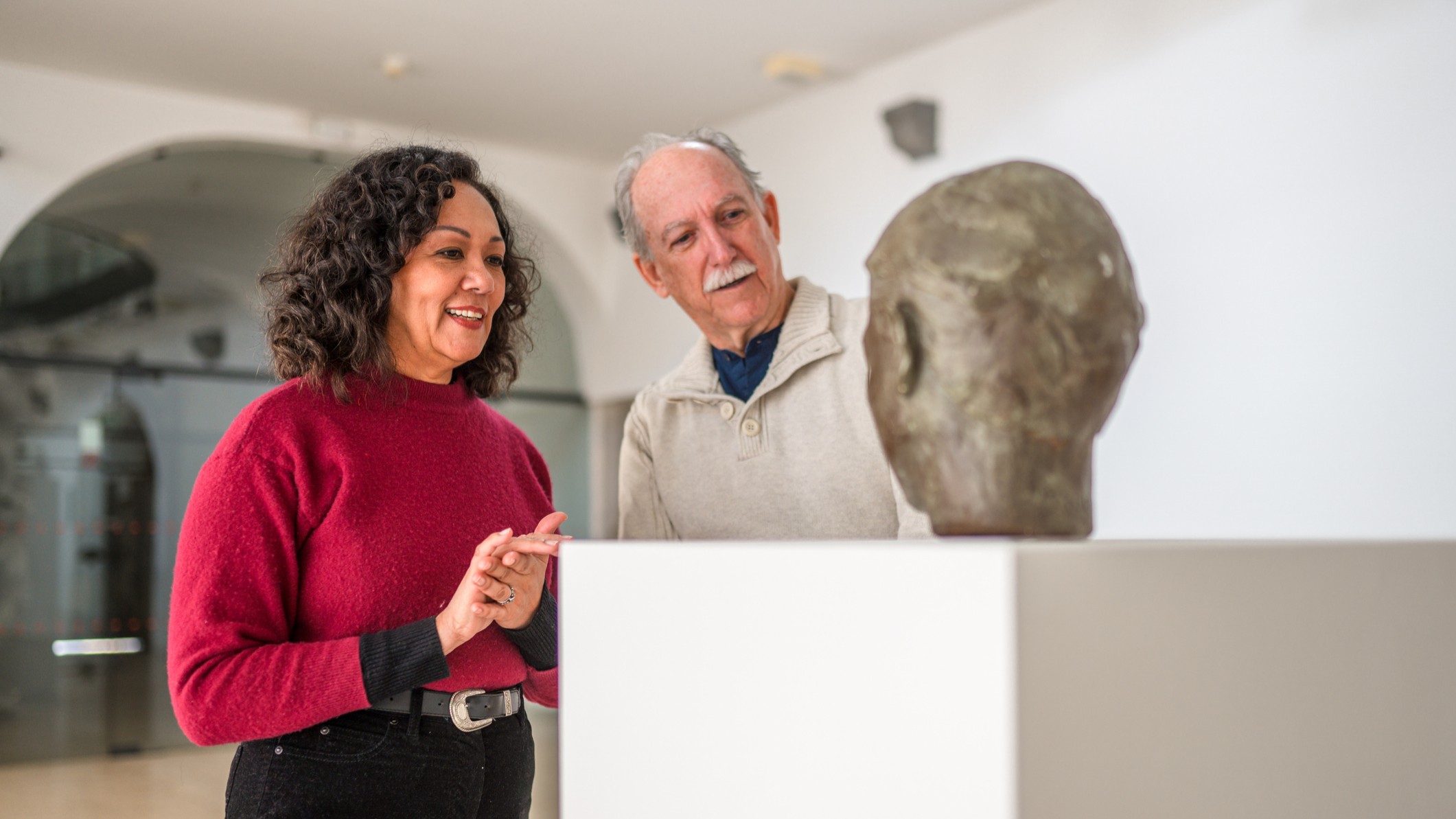 An older woman and man view a sculpture. They may be couple, or the woman may be a docent explaining the piece.