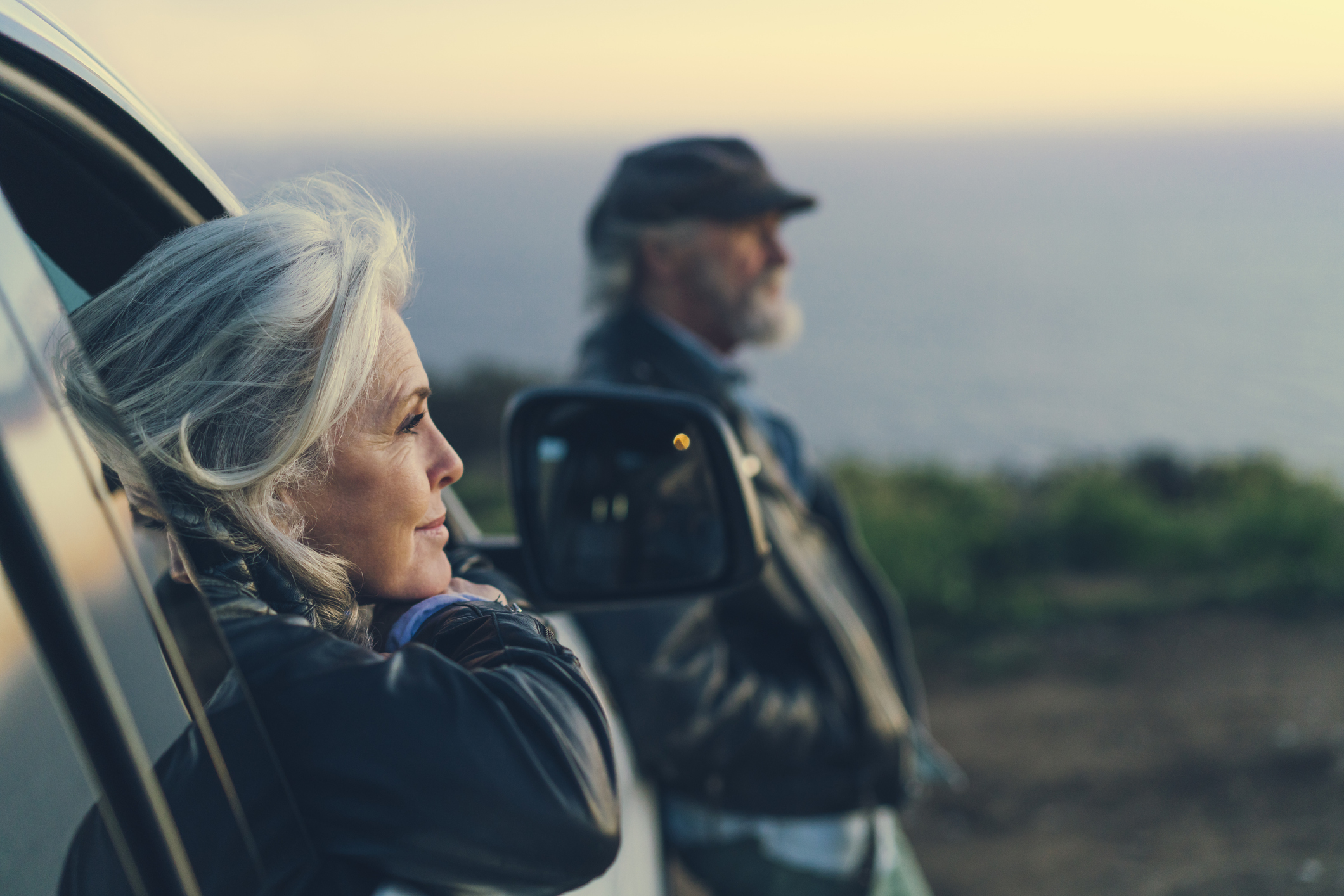 A mature woman sitting in the passenger seat of a car looks out at the horizon.