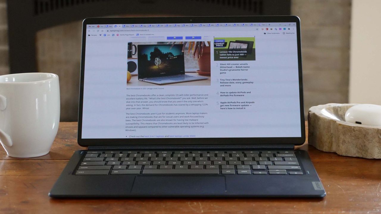 An open and powered on laptop sits on top of a wooden desk with a white mug to its left