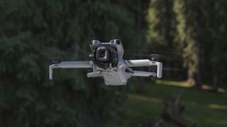 DJI Mini 5 Pro drone in flight, tree backdrop