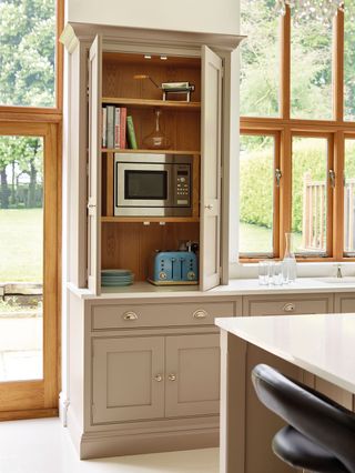 A light pink kitchen with white worktops and an open cabinet showing a microwave