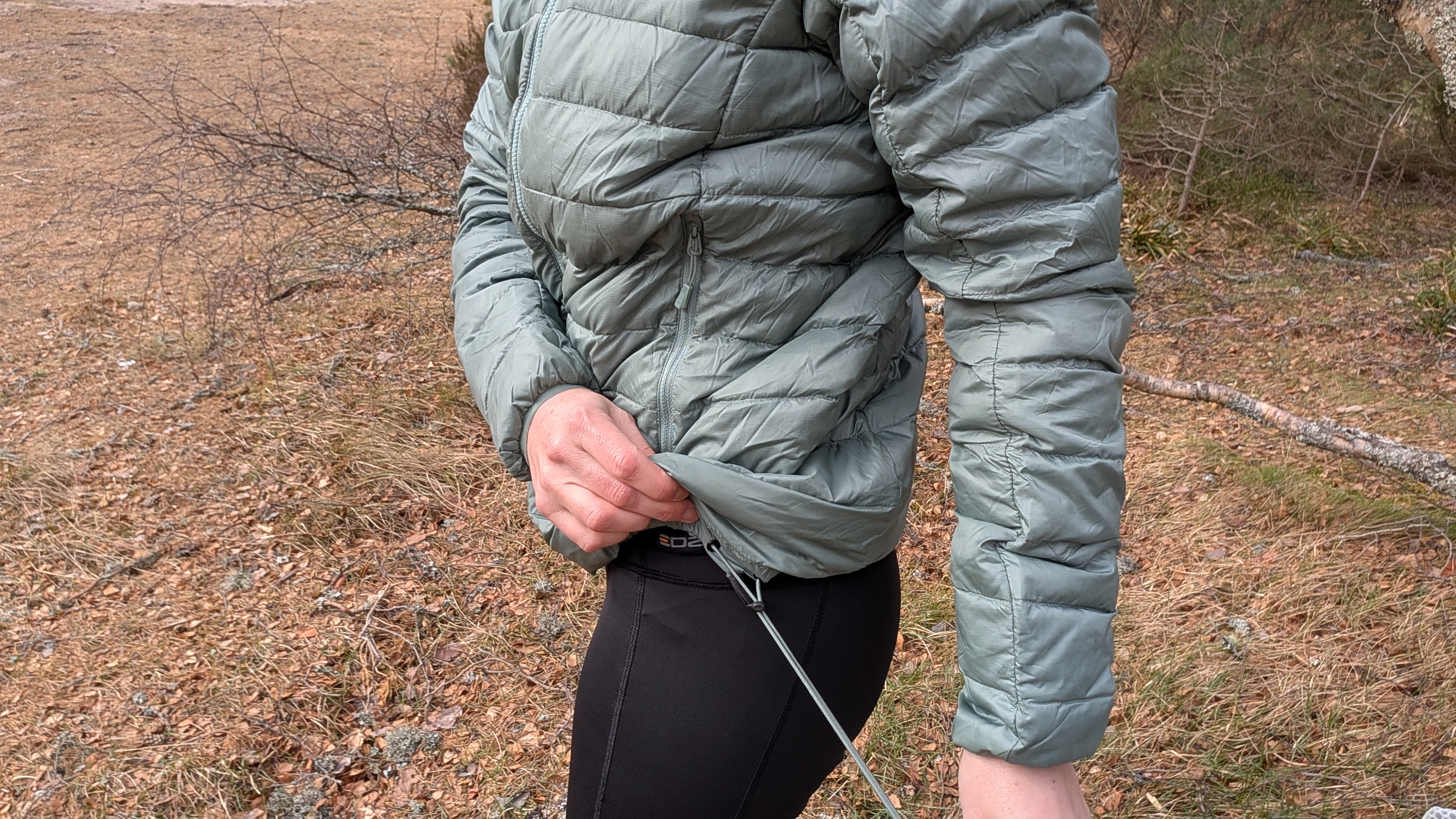 A woman showing the hem adjustment on a green down jacket