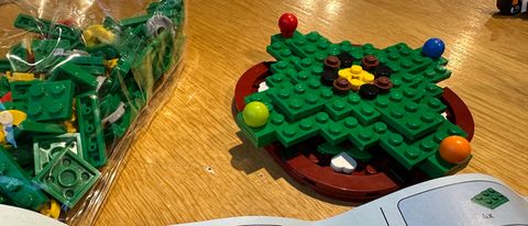Bottom layer of Lego Christmas tree built on wooden table with Lego pieces next to it