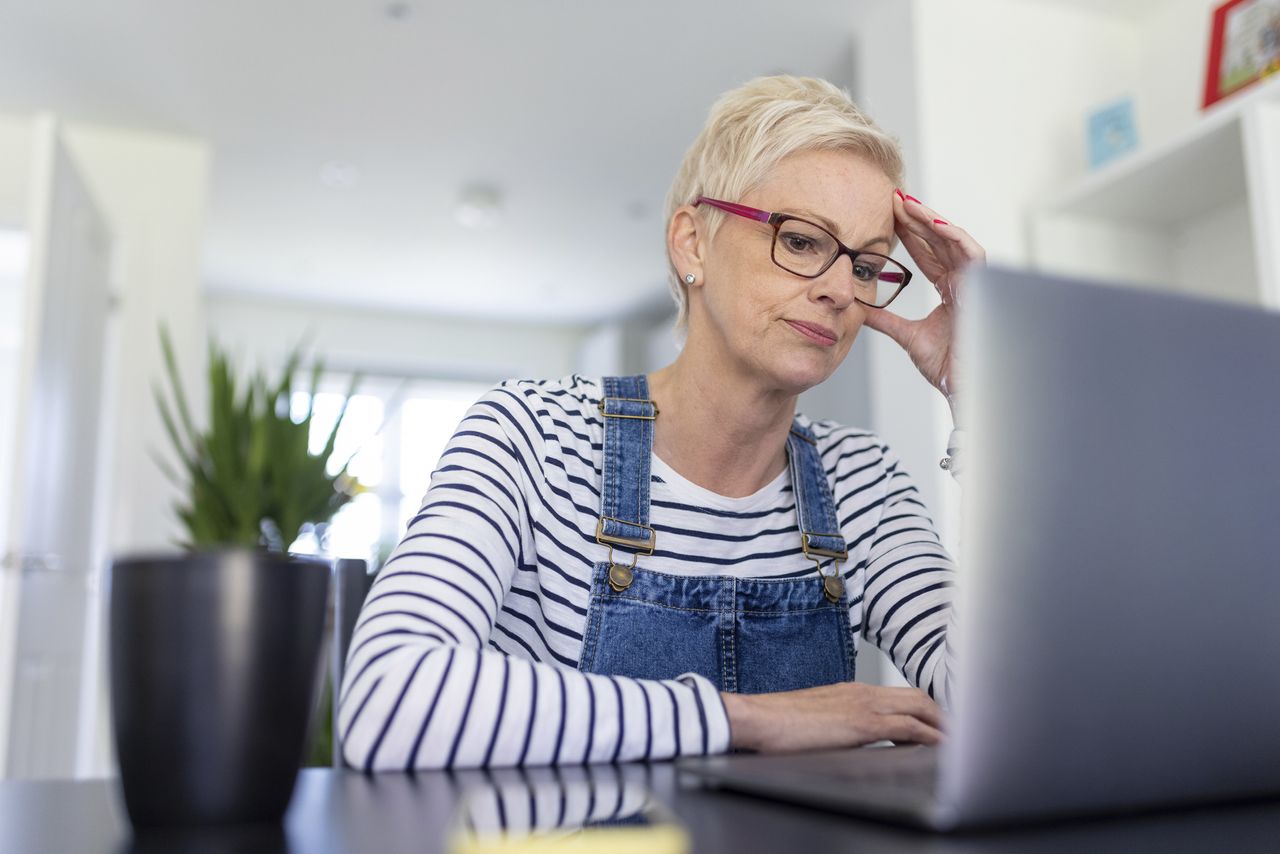 Worried businesswoman with head in hand while looking at laptop in home office