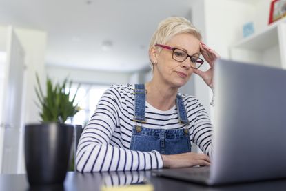 Worried businesswoman with head in hand while looking at laptop in home office