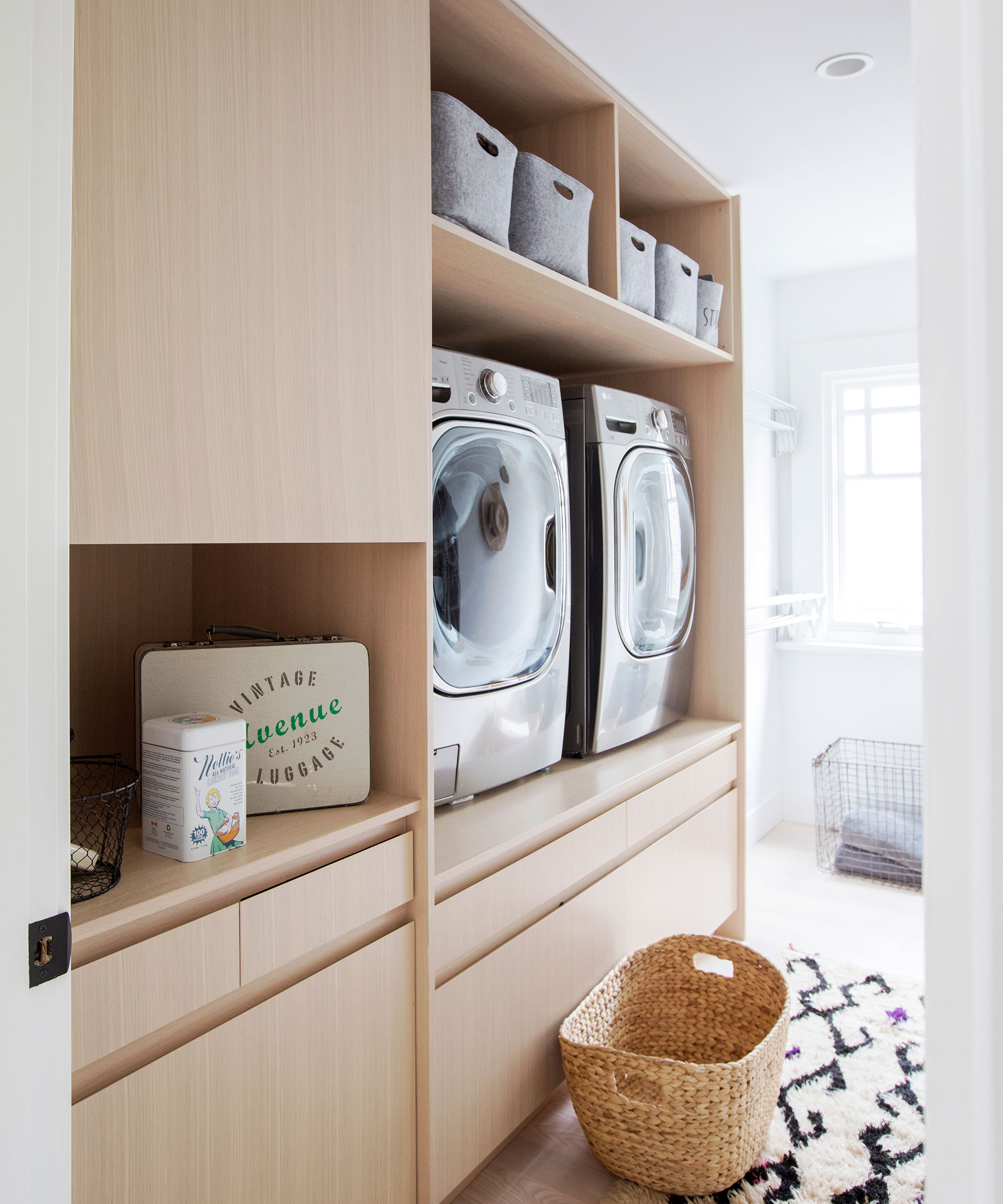 Small laundry room with built-in cabinetry for washer dryer and decorative rug on the floor beneath woven basket