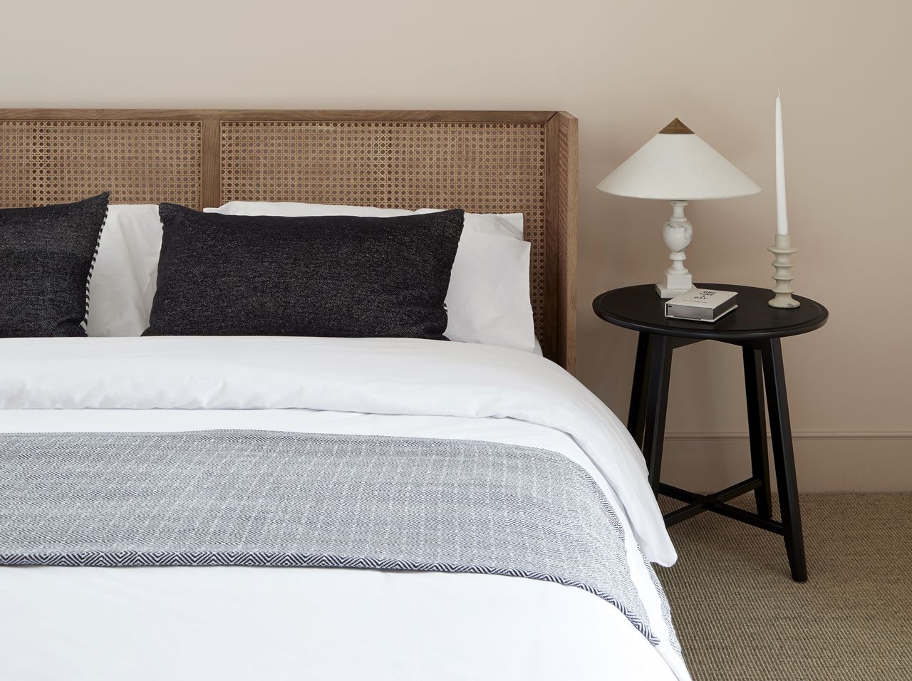 A bedroom with pink walls, a bed, a cane headboard, and a small side table