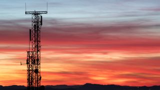A metal cell phone tower silhouetted against a pink and orange sunset