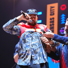 Travis Kelce puts on a jersey as he stands onstage with Rob Riggle and Paul Rudd during 2024 Big Slick Celebrity Weekend on June 01, 2024 in Kansas City, Missouri.