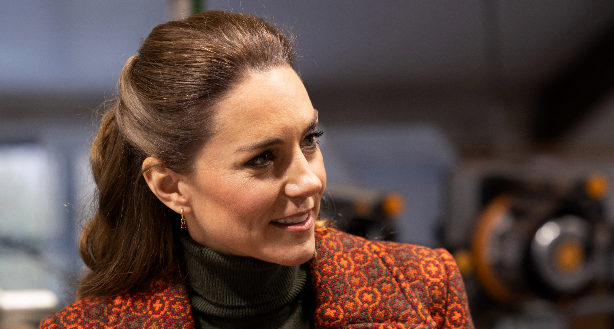 Princess Kate wearing an orange coat and green turtleneck turning to the side and smiling