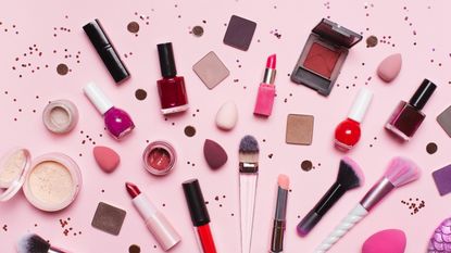 Top view of set of assorted tools and products for makeup application placed near shiny glitter on pink background