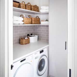 White utility room with white washing machine and tumble dryer, with shelves above