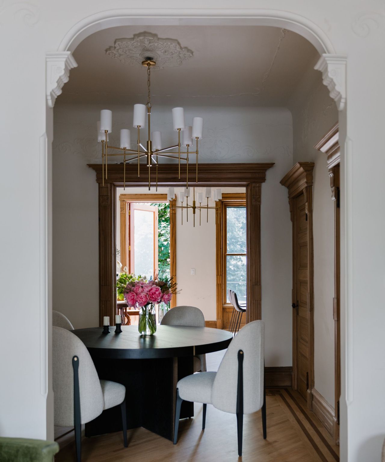 A brownstone dining room with a white molded arch and four white upholstered dining chairs
