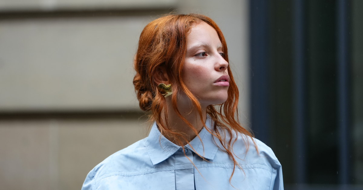 Face The Future A guest wears a full Patou outfit with a light blue button-up shirt with a structured collar and oversized chest pockets. Hair is styled in loose waves, and earrings are visible, outside Patou, on June 06, 2025 in Paris, France 