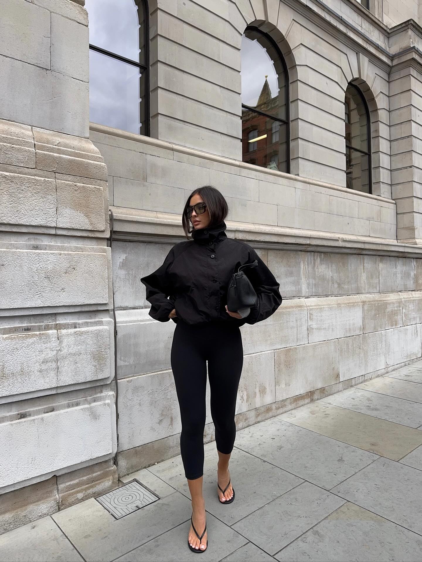 emma milton wears a black windbreaker jacket, capri trousers and heeled flip flops