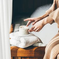 a woman in a tan robe applying a white cream to her hands