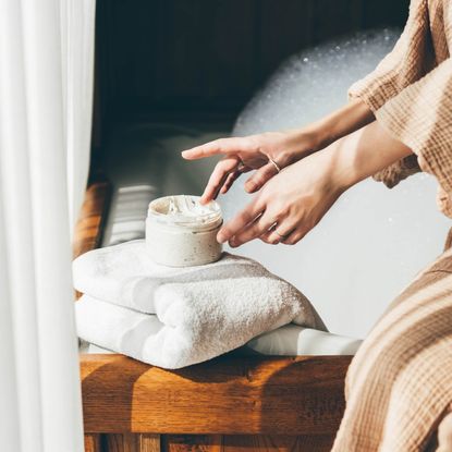 a woman in a tan robe applying a white cream to her hands