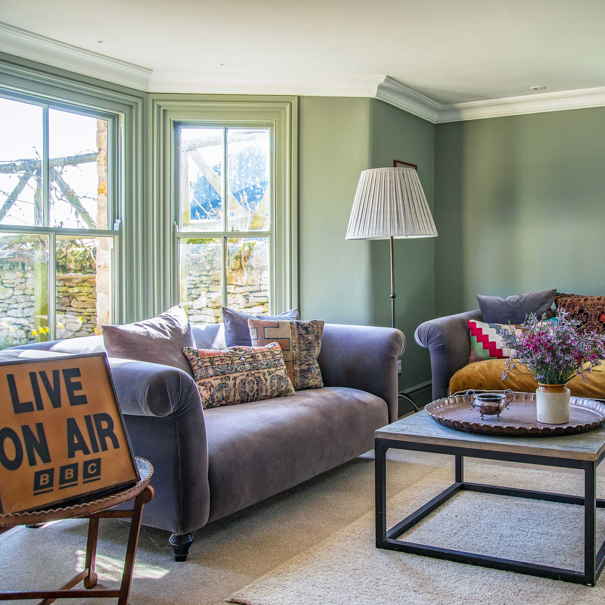 Green painted living room with large bay window, purple velvet sofas, mixed cushions, vintage accessories