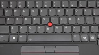 An extreme close up of a black laptop keyboard with a red dot in the center.