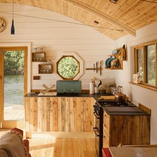 Luxury floating cabin at Dragonfly camping Pembrokeshire with wooden floor and counter, stove and oven and wooden wall shelves