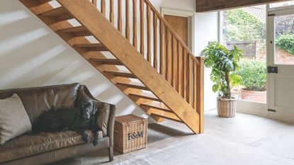 The double height stairwell in a barn conversion, a wooden staircase and banister, tiled flooring and glass windows and front door.