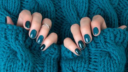 Two hands featuring blue nail designs/ pictured on a blue knitted background