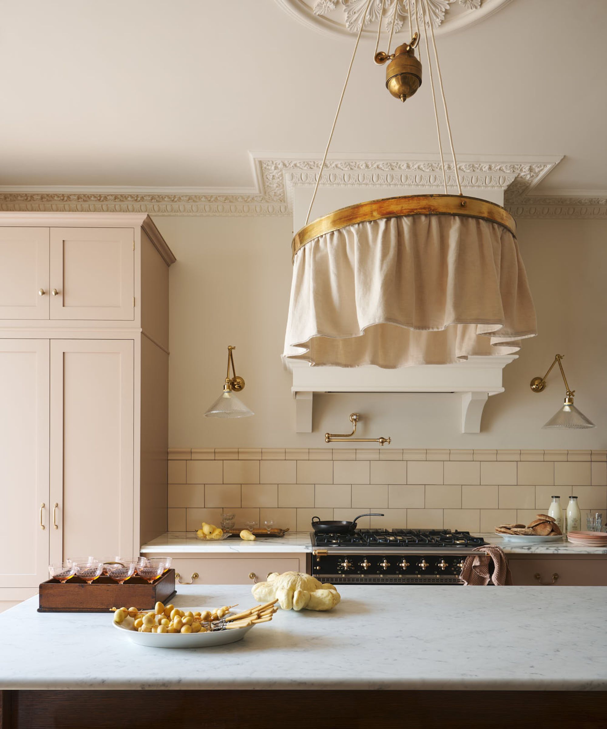 Cream kitchen by deVOL featuring pale cabinetry, marble countertops, brass accents, and a fabric pendant light above a large island.
