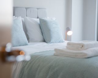 A set of white clean cotton towels are folded and place on a bed in a bedroom