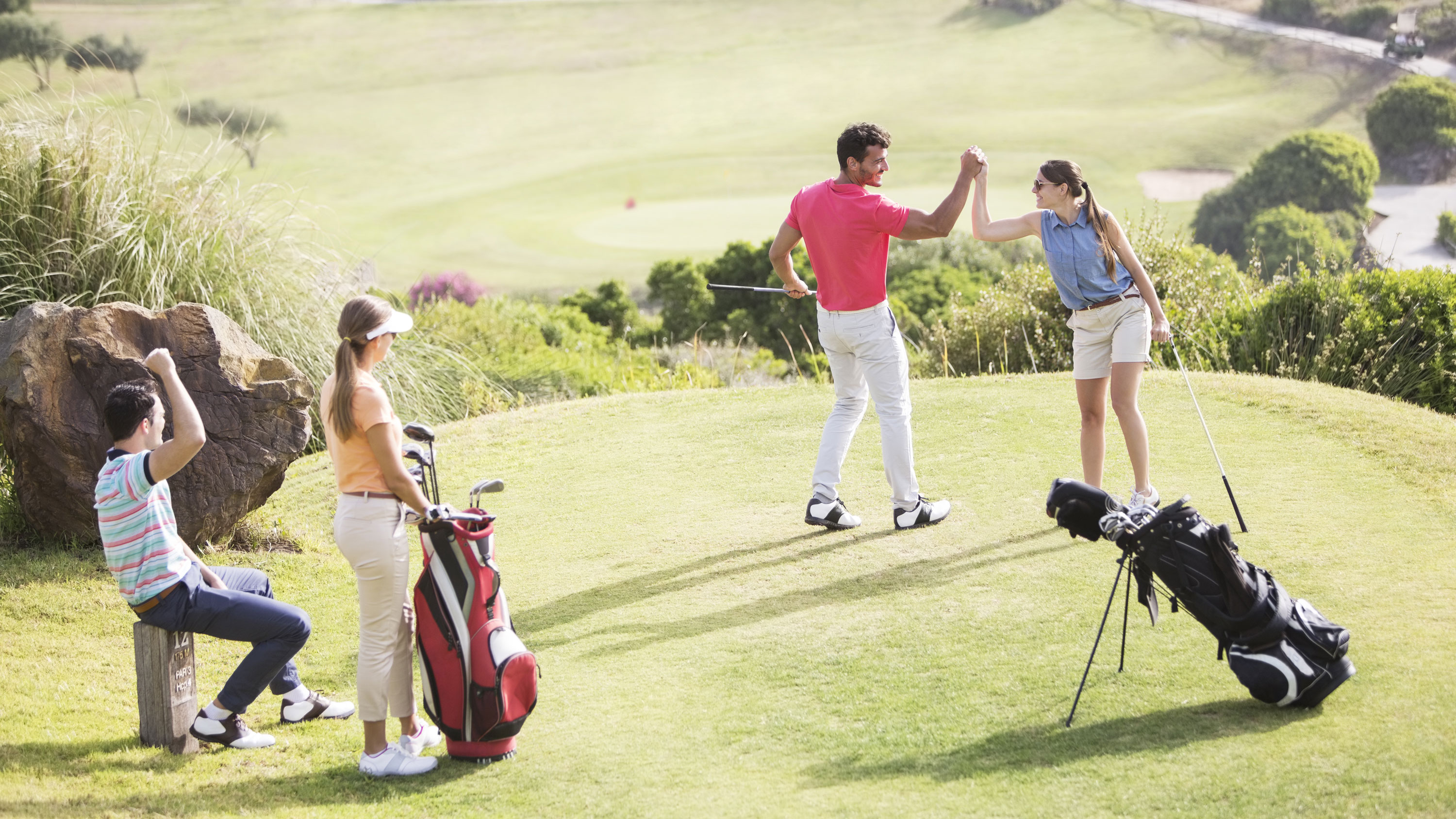 two golfers high fiving with two more golfers looking on