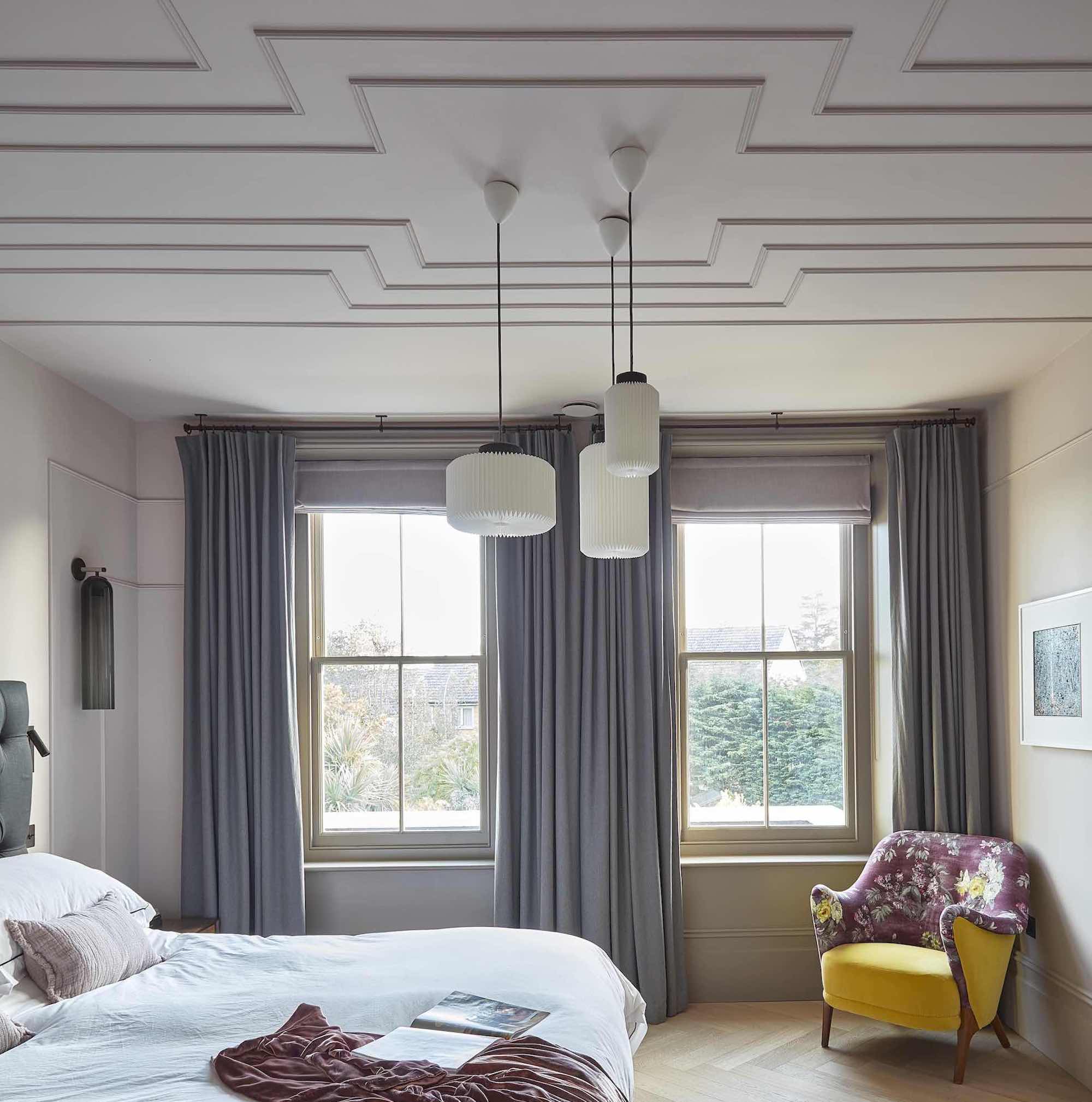 bedroom drenched in stone colour paint with double windows, white bed and yellow chair