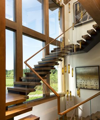 A stairwell with double height glass walls and walnut cantilevered steps