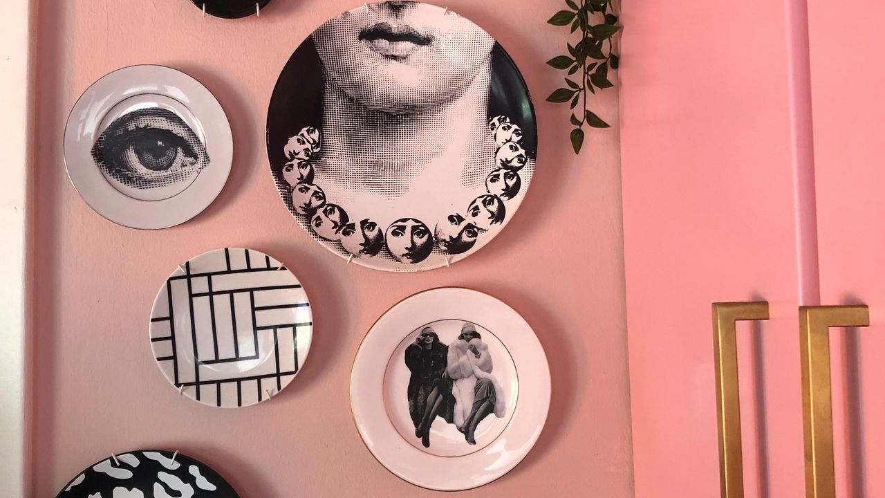 A pink cupboard with a pink-painted wall displaying a decorative plate gallery wall