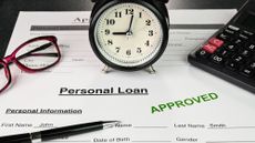 Paperwork for an approved personal loan sitting on a desk with an alarm clock, calculator, glasses, and pen on top of it