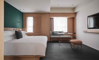 Kimpton Da An hotel room with pale timber panelling, teal wall behind bed and white linen, grey woven vinyl flooring